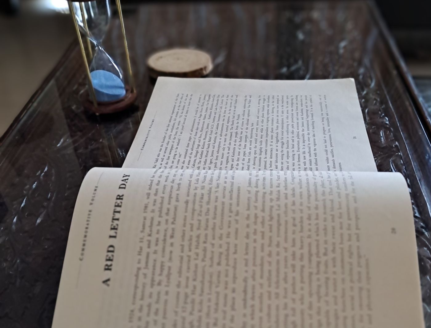 An open page of the commemorative volume for Lala Mulk Raj Saraf, headed 'A Red Letter Day', beside an hourglass